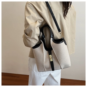Detail of canvas bag with black leather trim and gold twist lock clasp on a model