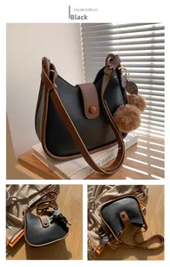 Detail van zwarte crossbodytas met bruine bies en pluchen balbedeltje in zonlicht