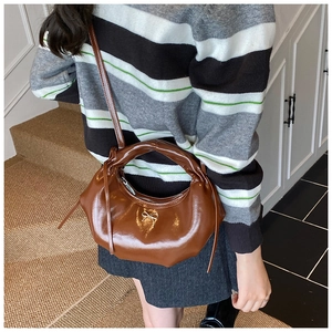 Détail d'un sac demi-lune marron verni avec un nœud argenté et une fine bandoulière