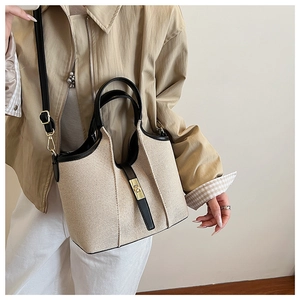 Close-up of beige canvas bucket bag with black leather trim and golden metal lock detail