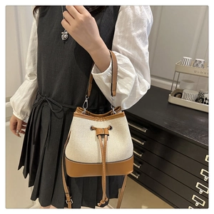 Detail of canvas bucket bag with brown leather trim and silver drawstring eyelets