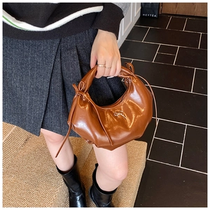 Détail d'un sac à bandoulière marron en forme de croissant avec des nœuds décoratifs