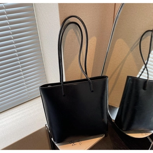 Close-up of minimalist black tote bag featuring polished leather texture and slim shoulder straps
