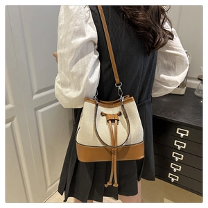 Detail of canvas bucket bag featuring caramel leather trim and adjustable shoulder strap