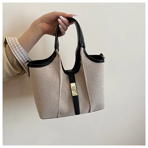 Detail of canvas tote bag featuring black leather trim and golden square swivel lock closure
