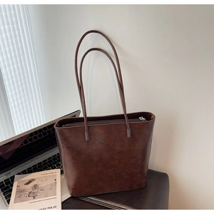 Detail of a dark brown vintage tote bag placed on a leather stool with a laptop