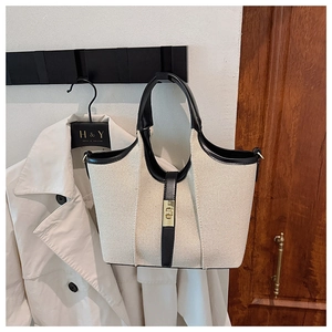 Close-up of cream canvas tote bag with black leather trim and golden twist lock on a hook