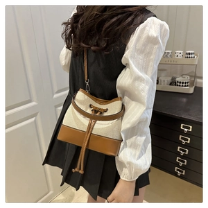 Detail view of canvas bucket bag with brown leather trim and drawstring closure