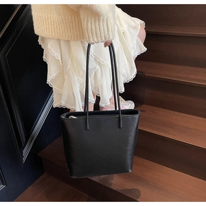 Close-up of minimalist black leather tote bag with slim shoulder straps on wooden stairs