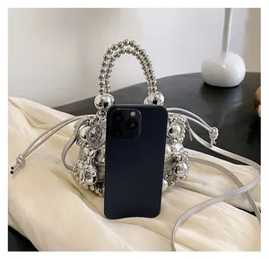 Size comparison showing silver beaded bucket bag next to a smartphone with drawstring