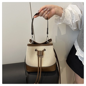 Detail of canvas bucket bag with brown leather trim and drawstring closure design