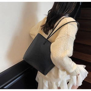 Minimalist black matte leather tote bag worn by a model on a shoulder with long straps