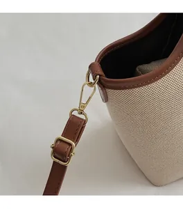 Close-up of golden hardware hooks and brown leather straps on canvas bucket bag
