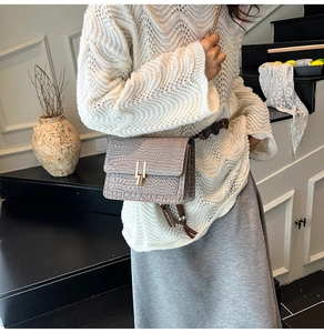 Detail of grey crocodile embossed crossbody bag with golden clasp and leather tassel accessory