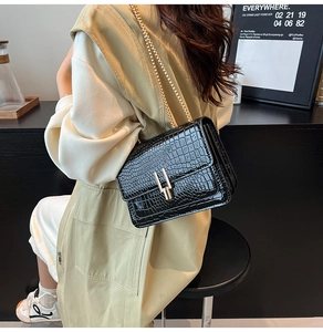 Close-up of black crocodile pattern leather bag with elegant gold chain and H-shaped buckle