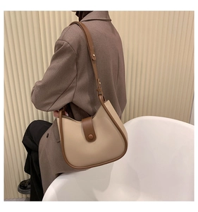 Model wearing a two-tone crossbody bag with beige leather and brown trim details