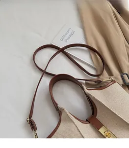 Detail of cream fabric and brown leather bag with golden metal turn-lock and strap