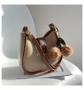 Detail of a chic beige bucket bag featuring brown leather trim and a fluffy charm