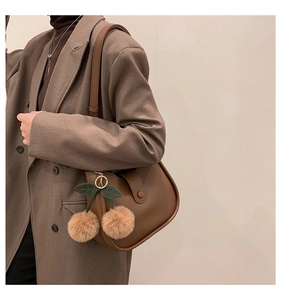Detail of dark brown matte leather saddle bag with a unique cherry plush charm accessory