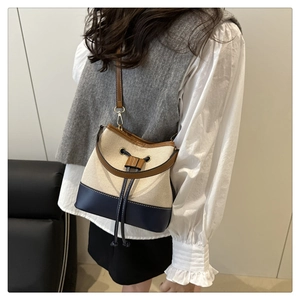 Detail of canvas bucket bag with navy leather base and drawstring closure on shoulder