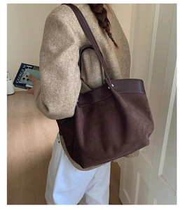 Detailed texture of dark brown suede tote bag with leather trim on wood floor