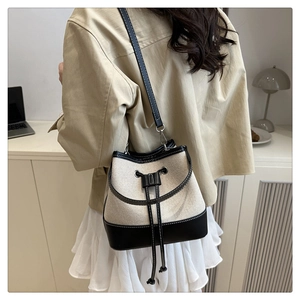 Detail view of canvas bucket bag with black leather trim and drawstring closure