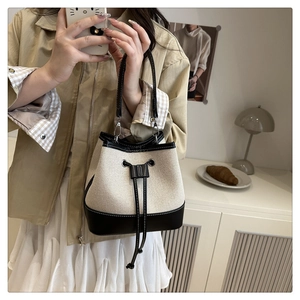 Detailed view of beige canvas bucket bag with black leather drawstring and trim details