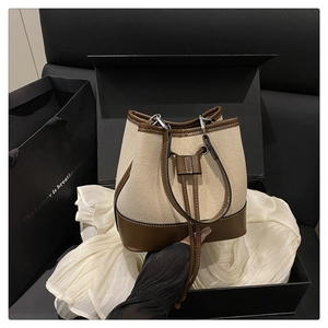 Detail of canvas bucket bag with leather trim presented in a premium gift box on white silk