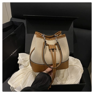 Close-up of canvas bucket bag with brown leather trim and silver metal buckle detail