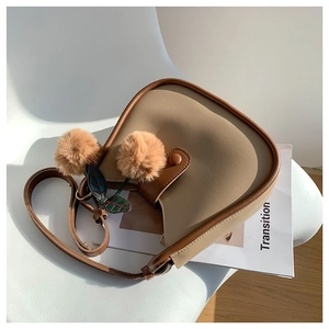 Minimalist beige and caramel saddle bag with plush cherry charm on a white chair