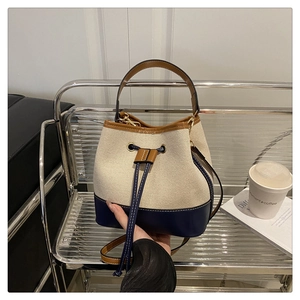 Minimalist canvas and leather bucket bag with drawstring closure on a silver display stand