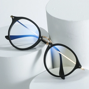 Retro round frame blue light blocking glasses with black and gold trim on white podiums