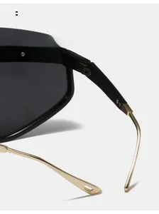 Close-up of black oversized sunglasses with gold metal curved legs and teardrop tips