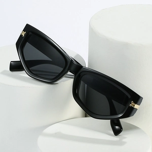 Lunettes de soleil œil-de-chat noires polies avec détails dorés sur socle blanc