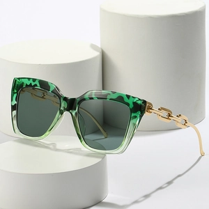 Green tortoise square oversized sunglasses with gold chain temples on white pedestal