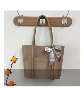 Detail of khaki pebbled leather tote bag featuring a front pocket and decorative silk scarf