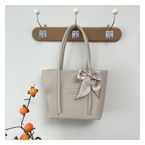 Detail of beige tote bag with litchi texture and elegant silk scarf on handle