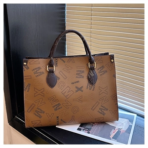 Detail of brown monogram tote bag with double handles and gold metal ring hardware
