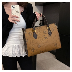 Detailed view of brown letter print tote bag with gold hardware on a model