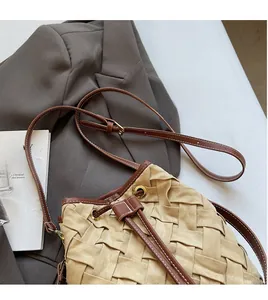 Detail of woven bucket bag featuring brown leather strap and gold adjustable metal buckle