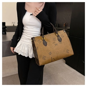 Detail of printed tote bag with MYXXINC logo and brown leather handles in indoor setting
