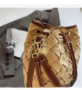 Detail of woven bucket bag featuring gold-tone hardware and brown contrast stitching