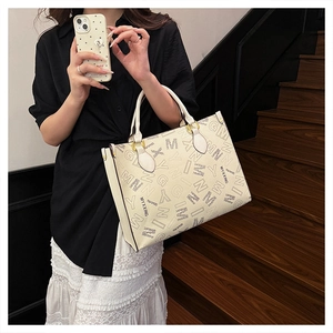 Detail view of large beige tote bag with black letter print and gold hardware hooks