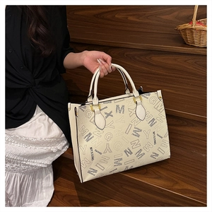 Close-up of printed lettering and golden hardware on the beige large tote bag