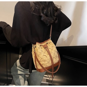 Detail view of woven bucket bag with brown leather trim on a model in interior setting