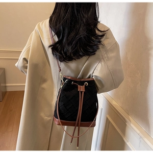 Detail of a black woven bucket bag with brown leather straps and gold metal accents