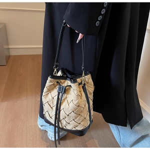 Detail of woven bucket bag featuring cream texture and black leather drawstring tassel