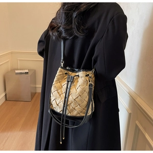 Chic woven drawstring bucket bag with black leather trim shown on a crossbody model
