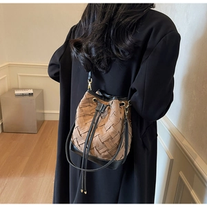 Detail of woven bucket bag featuring brown leather strips and black drawstring closure