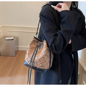 Detail of woven brown leather bucket bag with black drawstrings and metal eyelets